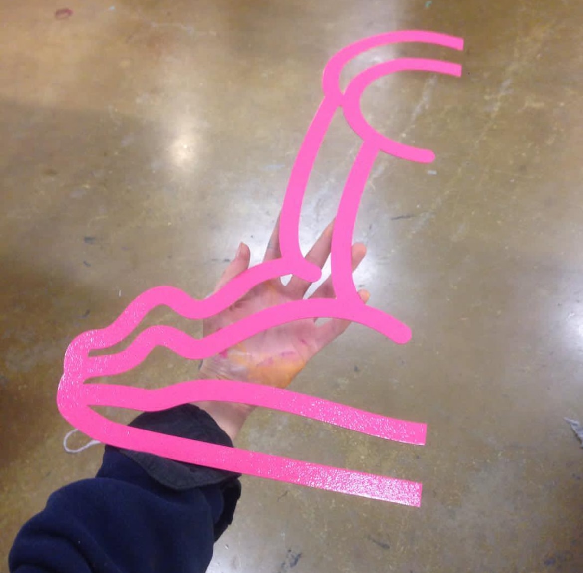 Hand holding bright pink foam letter sculpture on studio floor