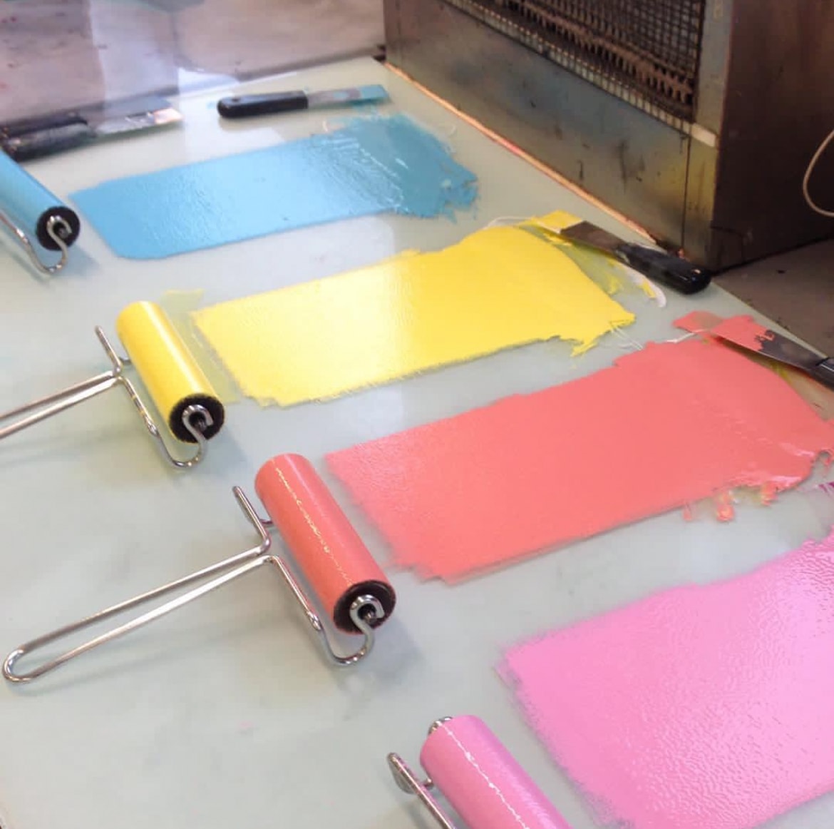 Ink rollers with blue yellow coral and pink paint swatches on glass