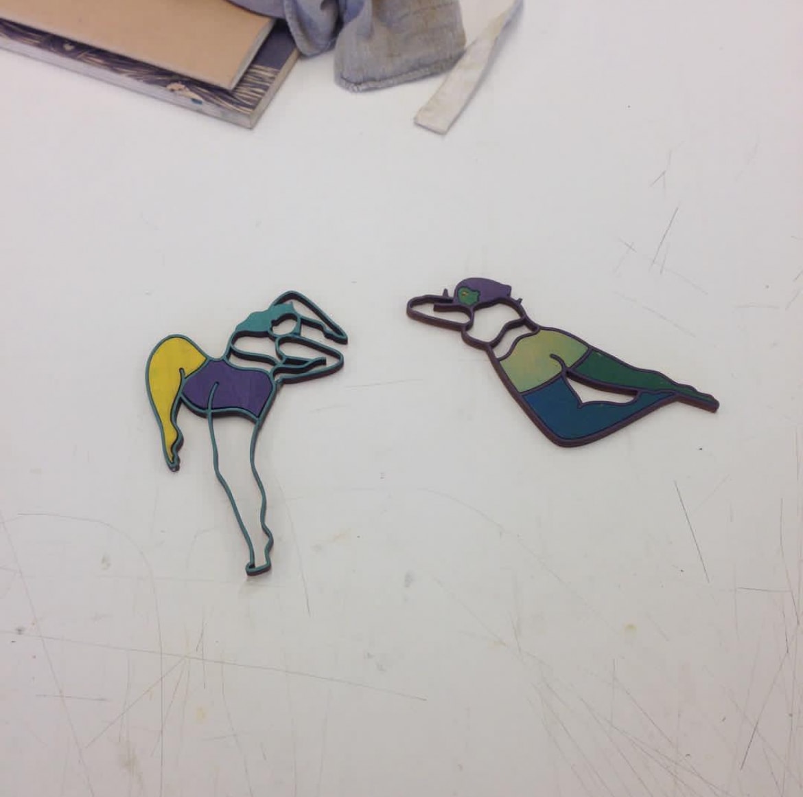 Two colorful laser-cut figure brooches on white studio table