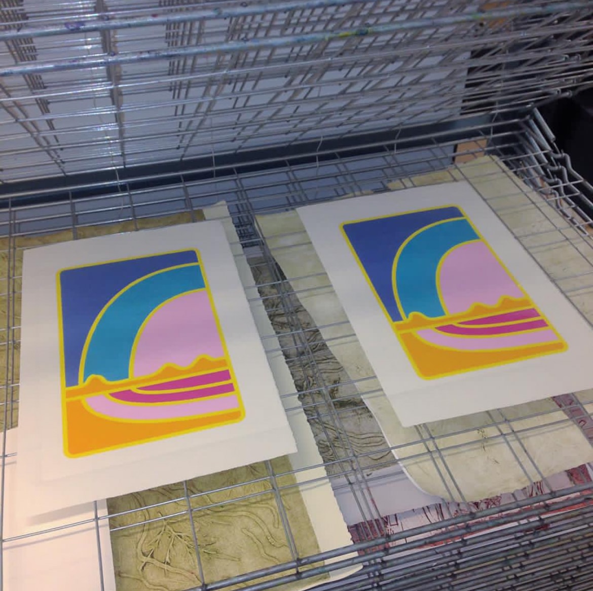 Two blue pink and yellow screenprints drying on rack