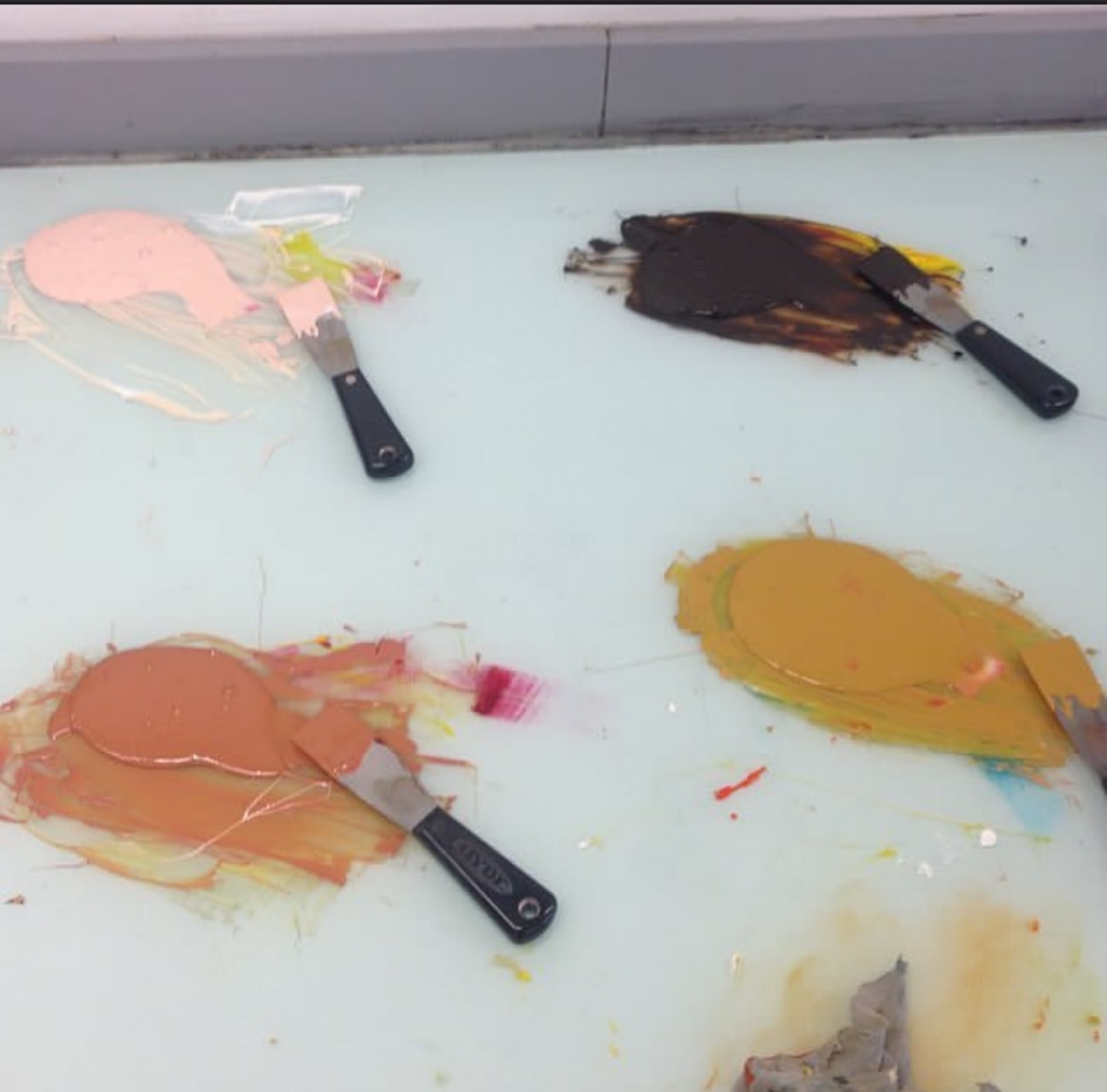 Paint swatches and palette knives on a glass surface